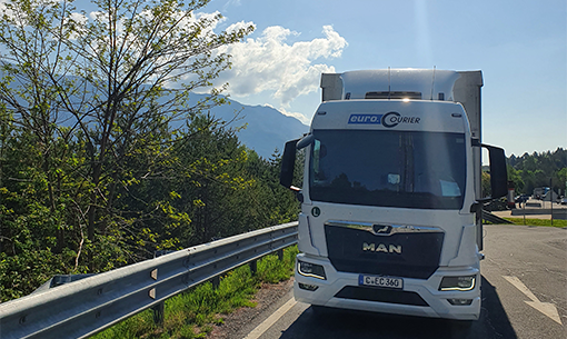 Unterwegs mit einem LKW irgendwo in Europa, im Hintergrund Bergkette zu sehen und die Sonne lacht.