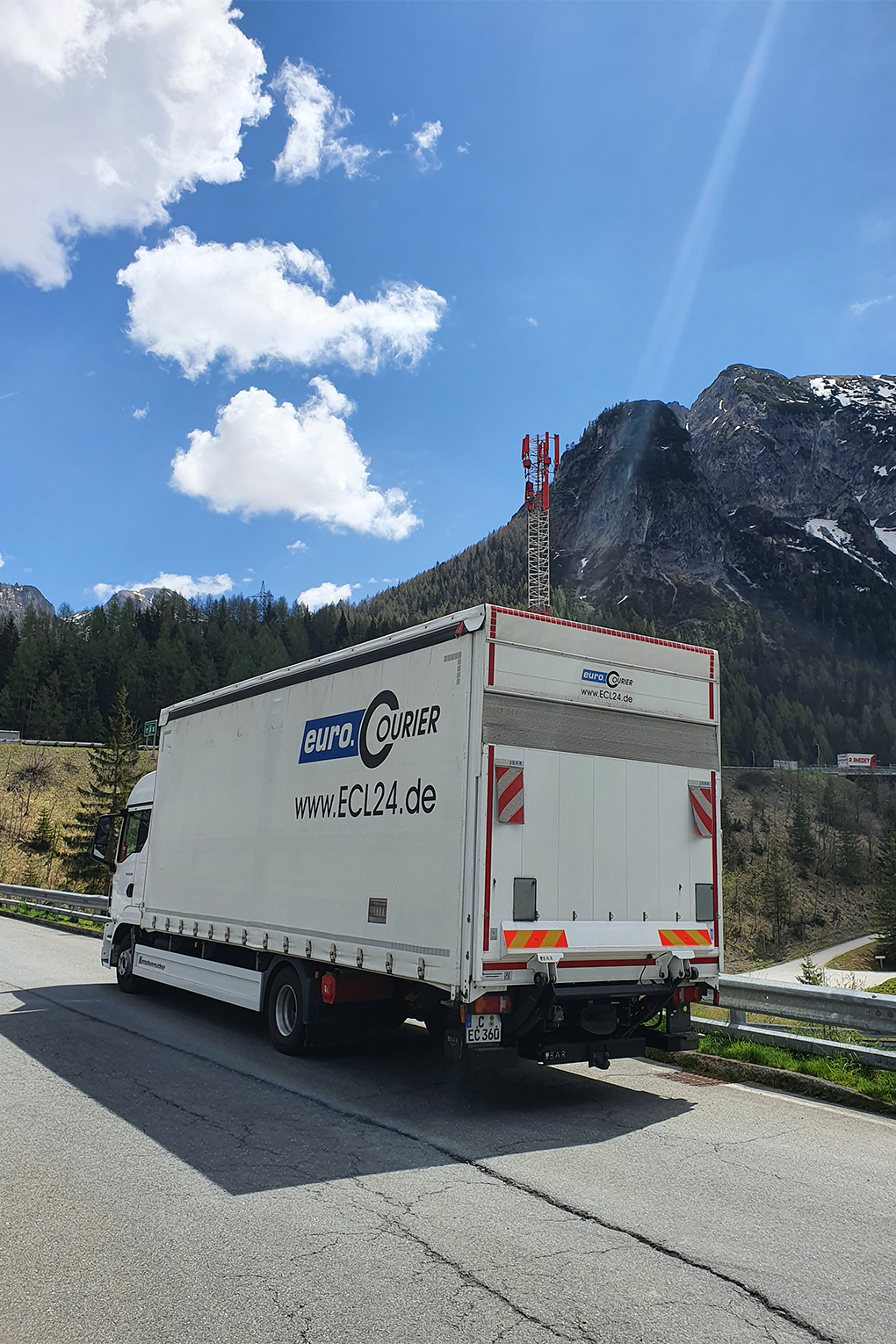 LKW von euro.COUIER von links hinten fotografiert, mit Alpen im Hintergrund bei strahlendem Sonnenschein.