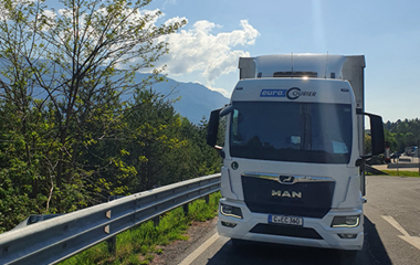 Unterwegs mit einem LKW irgendwo in Europa, im Hintergrund Bergkette zu sehen und die Sonne lacht.